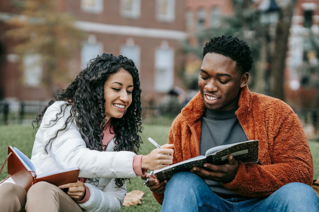 man and woman holding notebooks while sitting on grass