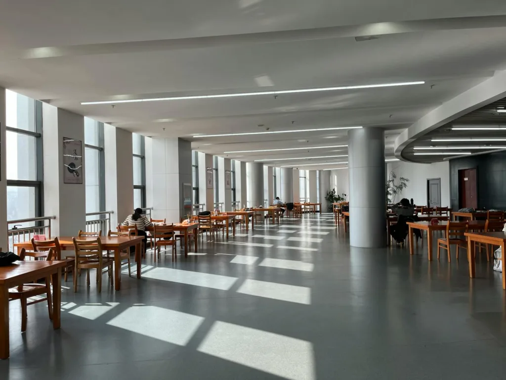 A modern university canteen in China with wooden tables and natural daylight streaming in.