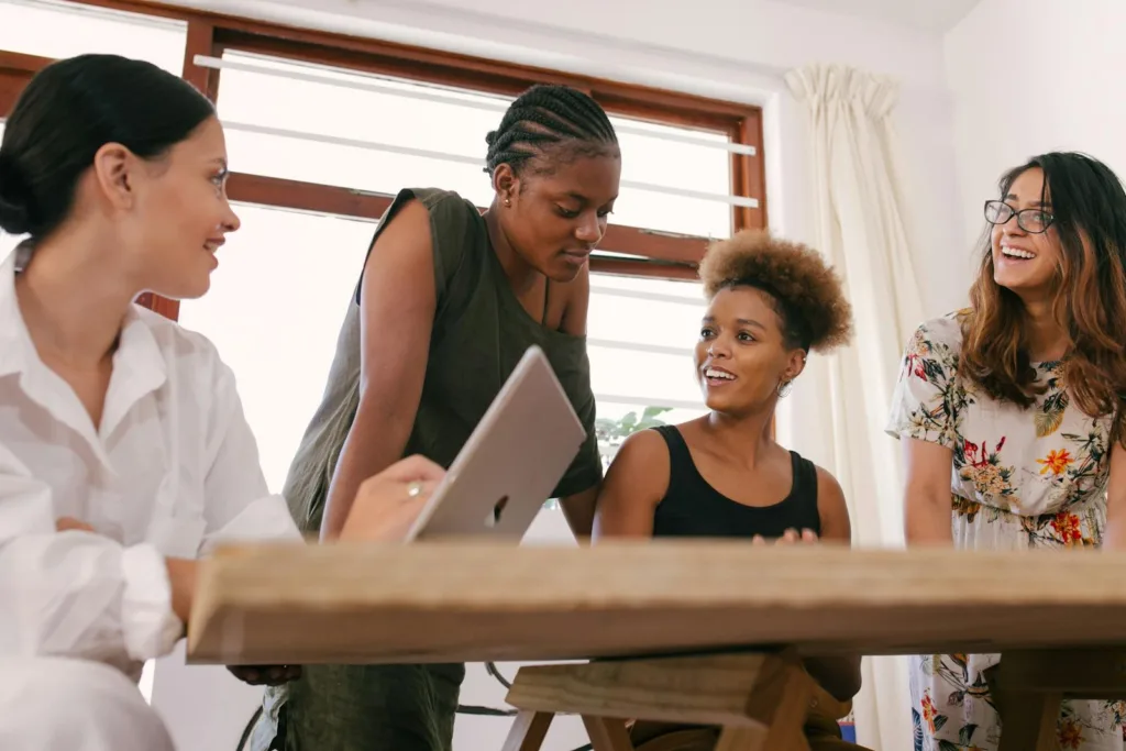 Four women in an office setting engaged in a lively creative discussion.