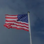 A vibrant American flag waving in the wind against a clear sky at Omaha Beach, France.